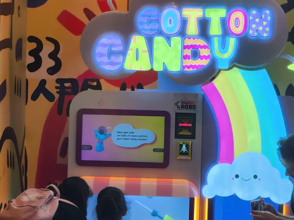 Gäste beobachten, wie der Sweet Robo Cotton Candy Automat vor Ort frische Zuckerwatte spinnt