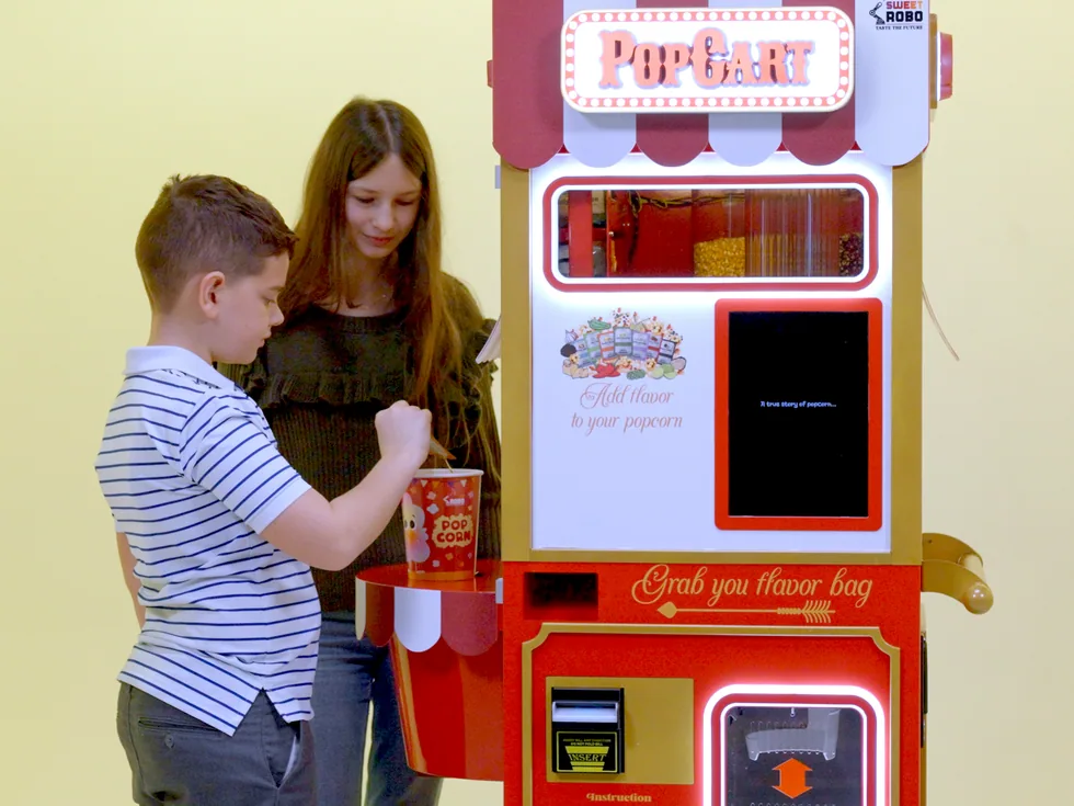 Kinder holen sich frisches Popcorn aus dem Sweet Robo PopCart Popcorn-Automaten